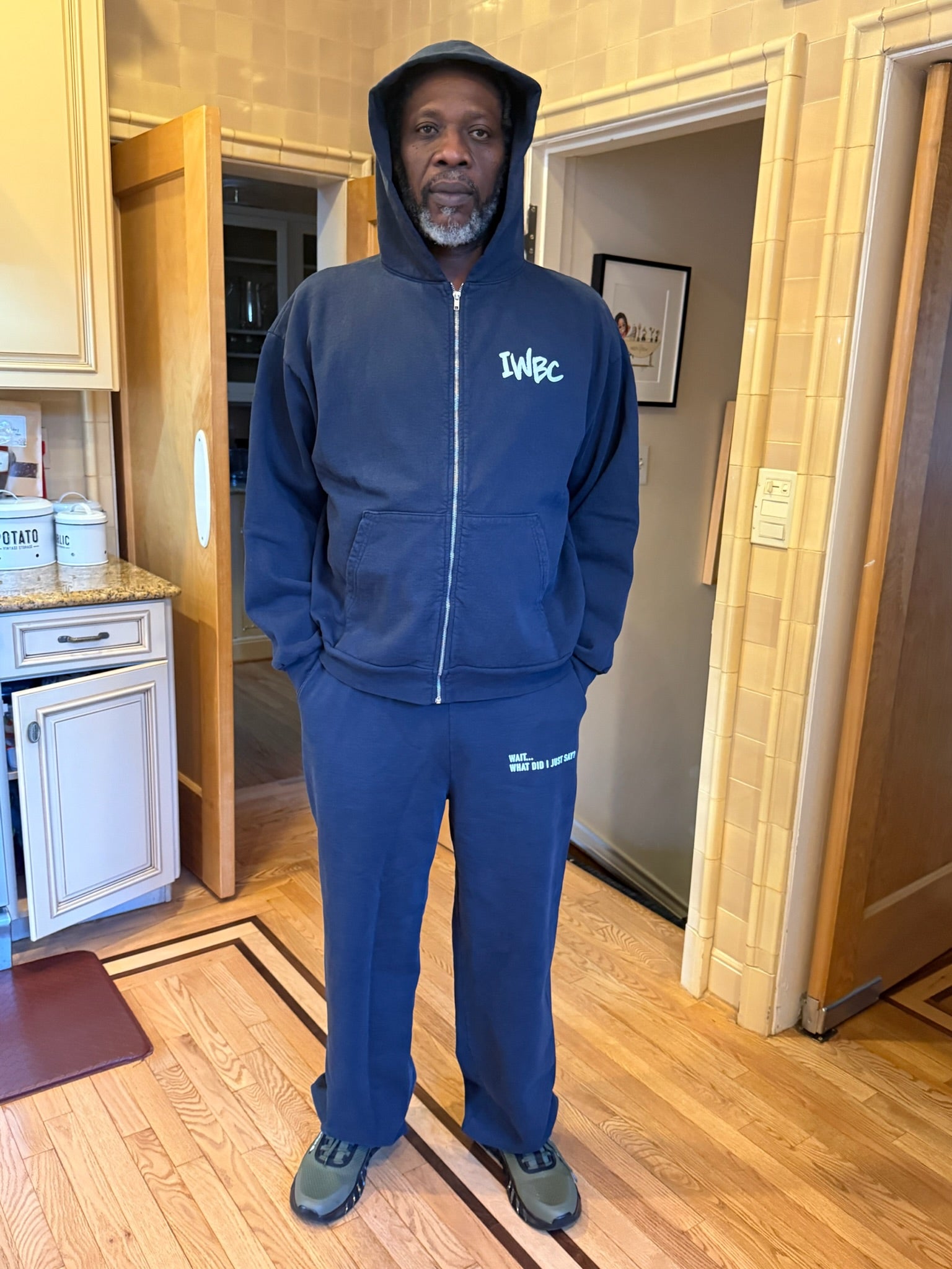 Man wearing a blue tracksuit with 'IWBC' branding in a home setting.