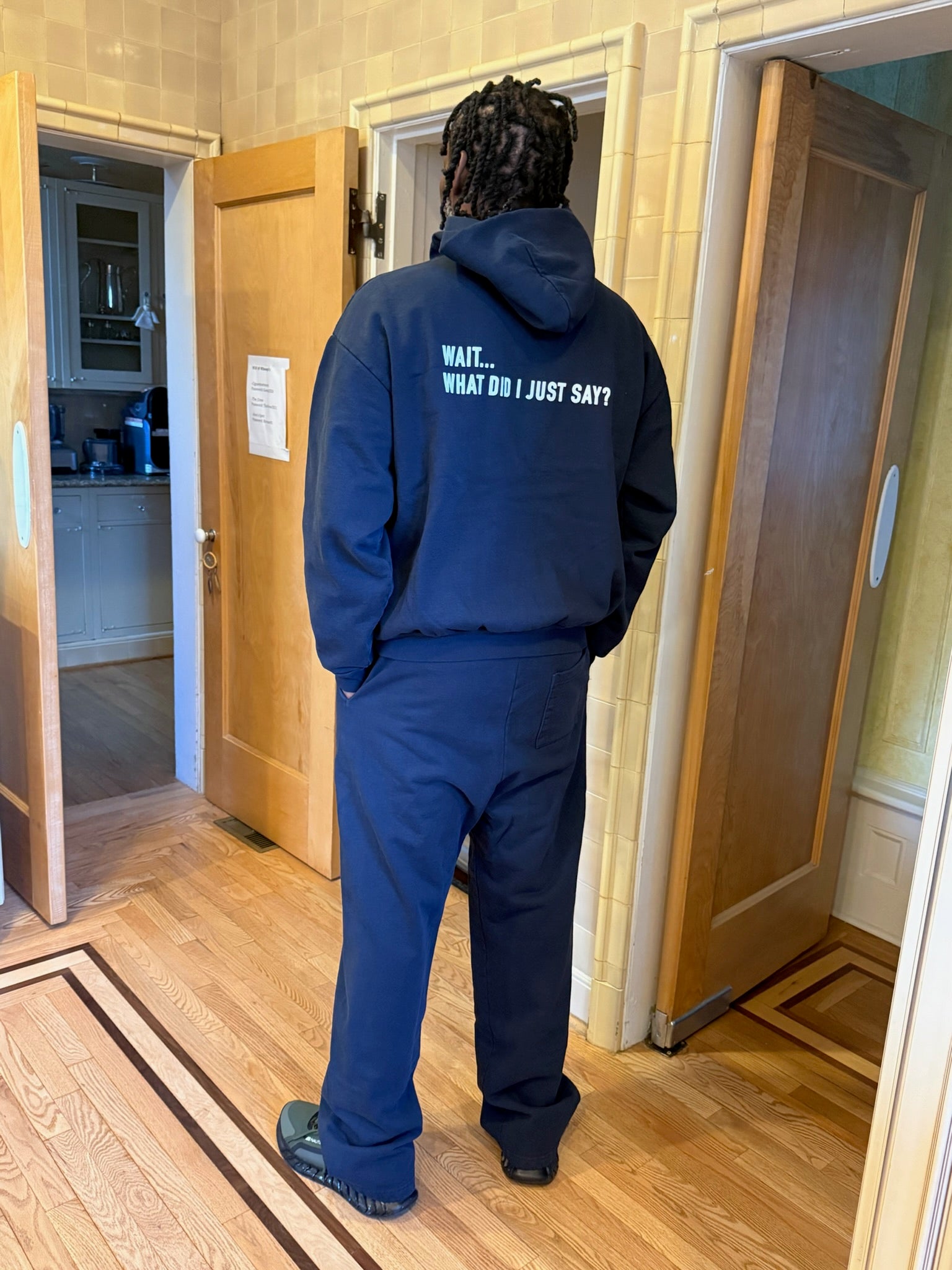 Person wearing a blue hoodie with text standing in a doorway.