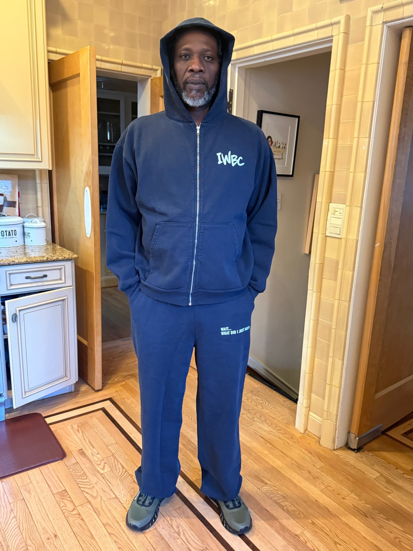 Man wearing a blue tracksuit with 'IWBC' branding in a home setting.