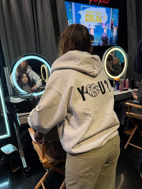 Person wearing a hoodie with 'YOU?' on the back in a salon setting.